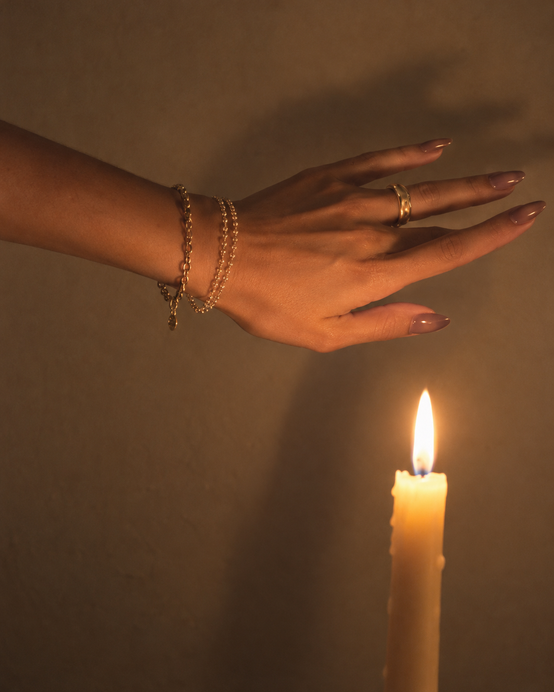Hand wearing press-on nails and gold jewelry beside a candle